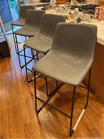 Four grey leatherette bar stools with black metal frames lined up at a kitchen counter, showing front and angled views.