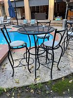 Side view of the black wrought iron round patio table and three chairs with beige cushions near pool area