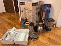 West Bend boxed coffee urn with food prep appliances and white hand mixer laid out on floor.