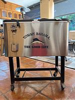 Front view of the Tommy Bahama metal cooler on wheels, showing the brand logo and bottle opener.