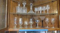 Wide view showing crystal decanters on top shelf, crystal stemware in front on middle shelf, and various bar glasses on lower shelf.