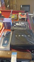 Tesla charging cable in black Tesla-branded case, multiple automotive accessories in original packaging on wood table
