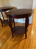 Front angle showing the oval shape, curved legs, and lower shelf of the dark brown wooden end table.
