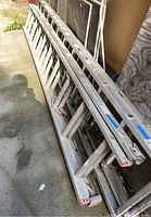 Aluminum extension ladder folded and resting on ground, showing length and structure with red end caps on feet and rails.