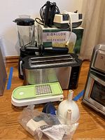 Overview of kitchen appliances and utensils including toaster, mandoline slicer, funnel attachments, mixers, and beverage dispenser box.