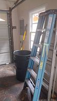 Image of the blue Werner fiberglass ladder standing folded near a garage door, showing overall ladder height and condition.