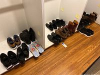 Wide view of various men's shoes lined up on the floor and a shelf, showing different styles and colors.