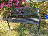 Front view of black metal outdoor bench with decorative scrollwork backrest, slatted seat, and curved armrests.