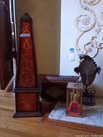 Tall wooden obelisk next to Asian crown display case, metal leaf sculpture, and wooden tray on floor
