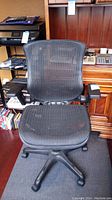 Front view of the black mesh office chair showing seat, mesh backrest, and caster wheels base.