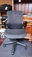 Front view of black mesh office chair with armrests and five-wheel base showing mesh seat and backrest.