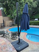 Full view of the patio cantilever umbrella positioned beside pool with navy blue canopy closed and base on a stone patio.