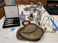 Overview of all lot items together on kitchen island, showing butter spreaders in box, oil lamp, perfume bottle, brass leaf dishes, Washington DC dish, decorative pitcher vase and brass plate easels