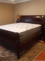 Side angle showing dark wood sleigh bed frame with curved headboard and footboard, queen mattress in place