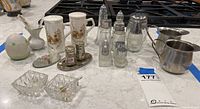 Overview of all pieces including ceramic shakers, glass and metal shakers, crystal salt cellars, and cream pitchers on countertop.