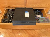 Drawer view showing PS4 console centered, cable bundles on left and right, stack of game cases