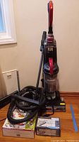 Front view of Eureka Pet Pal Turbo upright vacuum with hose attachments coiled beside it and boxed Shark powered scooper and Turbo steam iron on the floor.