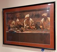 Framed lithograph showing four chefs in white hats working behind a kitchen counter, warm earth tone color palette, black frame with reddish-brown mat.