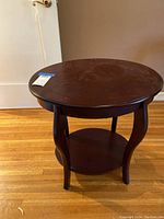 Front angle of the round dark brown wooden end table showing the top surface, curved legs, and lower shelf.