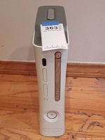 Front and side view of white Xbox 360 console showing power button and disc tray with seller tag on top.