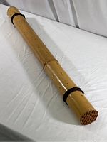 Full length view of 32 inch bamboo rain stick laid on white surface, showing polished bamboo surface and twine grip near ends.