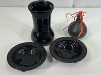Photo showing one black glass vase, painted gourd with orange ribbon, and two footed black glass dishes with embossed floral design in front.