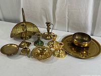 Collection of brass and metal items including candlesticks, basket, small dishes, bowl, and round platter shown on white surface.