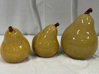 Three ceramic pears arranged side by side, varying sizes, tan glazed with a natural crackle glaze finish and brown stems.