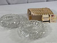 Two clear heavy crystal ashtrays approximately 6 inches in diameter beside a box containing numerous vintage unused Copacabana matchbooks.