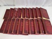 20 red hardbound vintage books arranged side-by-side, spines visible, displaying 'The Book of Knowledge' title with decorative gold accents, showing signs of wear and aging.