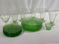 Photo showing collection of five juice glasses, one stemmed fruit cup, one small serving cup, and stacked plates in light green Depression glass.
