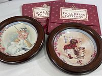Two Hamilton collectors plates in wood display frames and two American Girl doll dress pattern kits shown in red covers.
