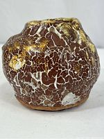 Front view of the pottery vessel showing rounded shape and crackled brown, white, and yellow glaze patterns.