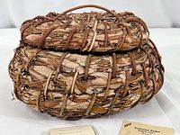 Close-up of the woven oval basket showing natural bark and branch materials used in construction.