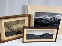 Three black and white landscape photographic prints arranged on a white cloth background; two framed without glass and one mounted on board