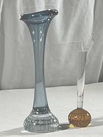 Tall blue-gray blown glass bud vase with wide flared rim and heavy air bubble infused clear base next to shorter amber air bubble base vase with clear stem