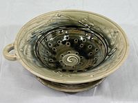 Side view of ceramic colander nested in matching saucer showing handle and drainage holes