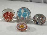 Four rounded art glass paperweights on white background showing variety of internal colorful floral and abstract patterns.