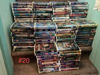 Stacked VHS tapes on stairs showing a large collection including titles like Hercules, Mulan, Bambi, and 101 Dalmatians among others. Most tapes in standard VHS plastic cases with visible wear on some cases.