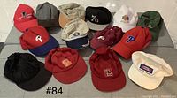 Lot of 14 baseball caps arranged flat on a surface to show variety and logos.