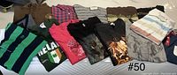 14 men's large shirts including various tees, polos, and sweaters, laid out on a bed showing front designs and colors.