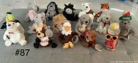 Front view of all 16 plushies laid out on a flat surface showing variety of Coca-Cola characters and animals.