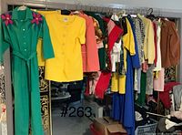 Green jumpsuit with pink flowers, yellow jacket and skirt, and assorted hanging vintage clothes.