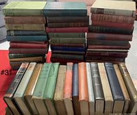 Photo showing a large stack of older hardcover books with one layer of books standing upright in front and three large stacks behind.