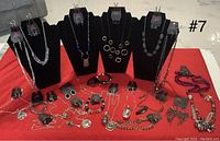 Photo of multiple black jewelry display stands holding silver-tone and black-tone necklaces along with several pairs of earrings hung on tags and two bracelets laid flat on a red cloth.