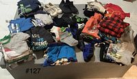 Overview of various boys' clothing including multiple shirts, pants, shorts, socks and footwear arranged on the floor.