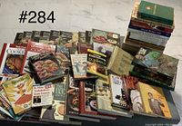 Mixed collection of hardcover and softcover books with various cooking and gardening topics arranged on a surface, showing some wear and sticker prices.
