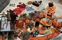 Photo showing a variety of Halloween decorations including pumpkin figurines, a large lit Halloween pumpkin, and several small Halloween-themed items arranged on an orange and black table cloth.
