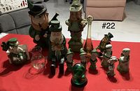 Multiple Irish St. Patrick's Day themed figurines grouped on a red cloth including leprechauns, a glass tumbler, and decorative vases.
