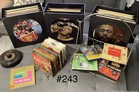 Full view of three black LP holders, 45 records in plastic holder, metal magazine rack, reel to reel tape and some LPs